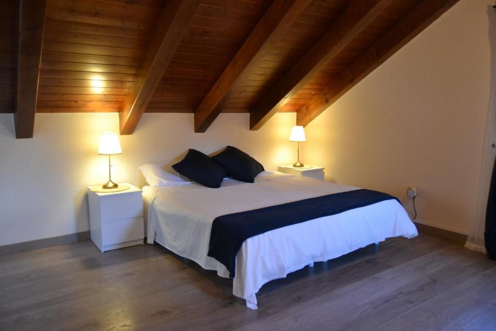 Dormitori amb sostre inclinat de fusta. Llit amb roba de llit blanca, dues tauletes de nit amb làmpades. Terra de fusta.