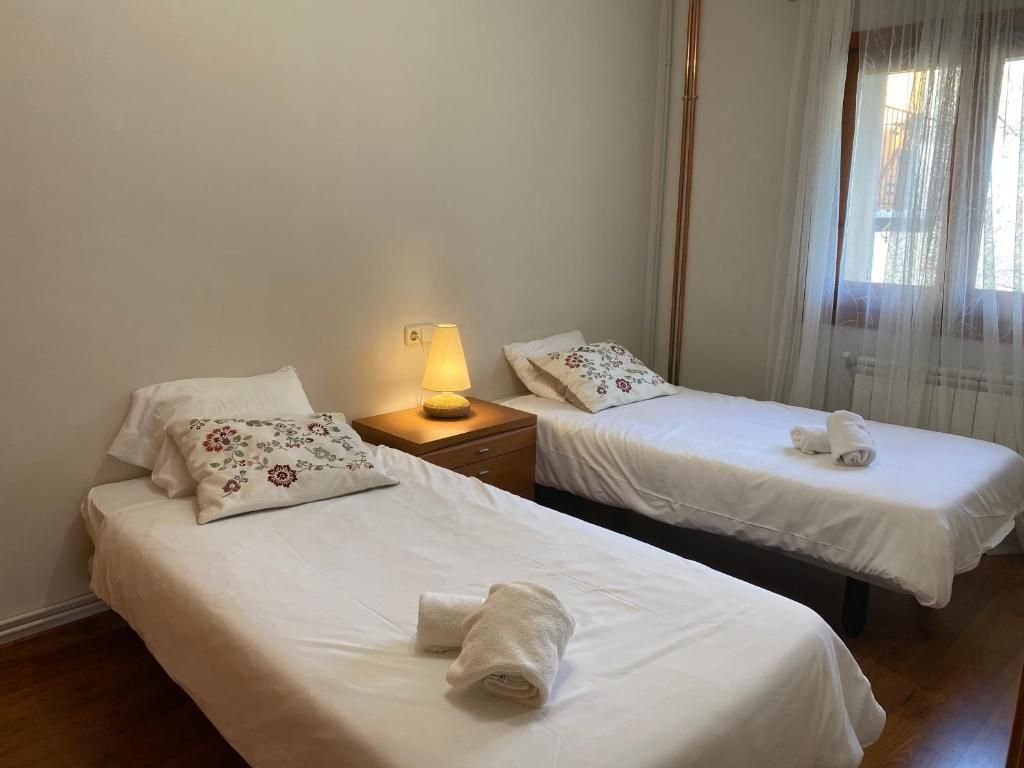 Dos llits individuals en una habitació amb tauleta de nit i una finestra amb cortines blanques.