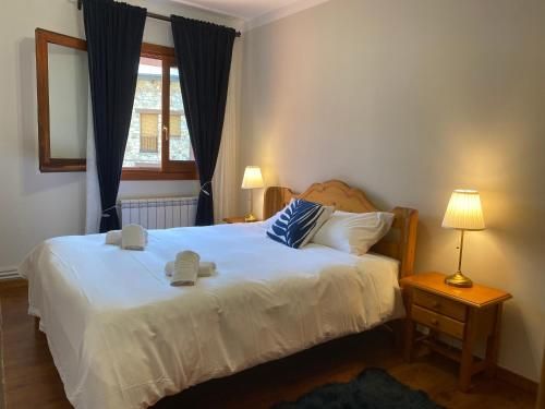 Dormitori amb un llit, tauletes de nit, làmpades, finestra amb cortines i tovalloles.