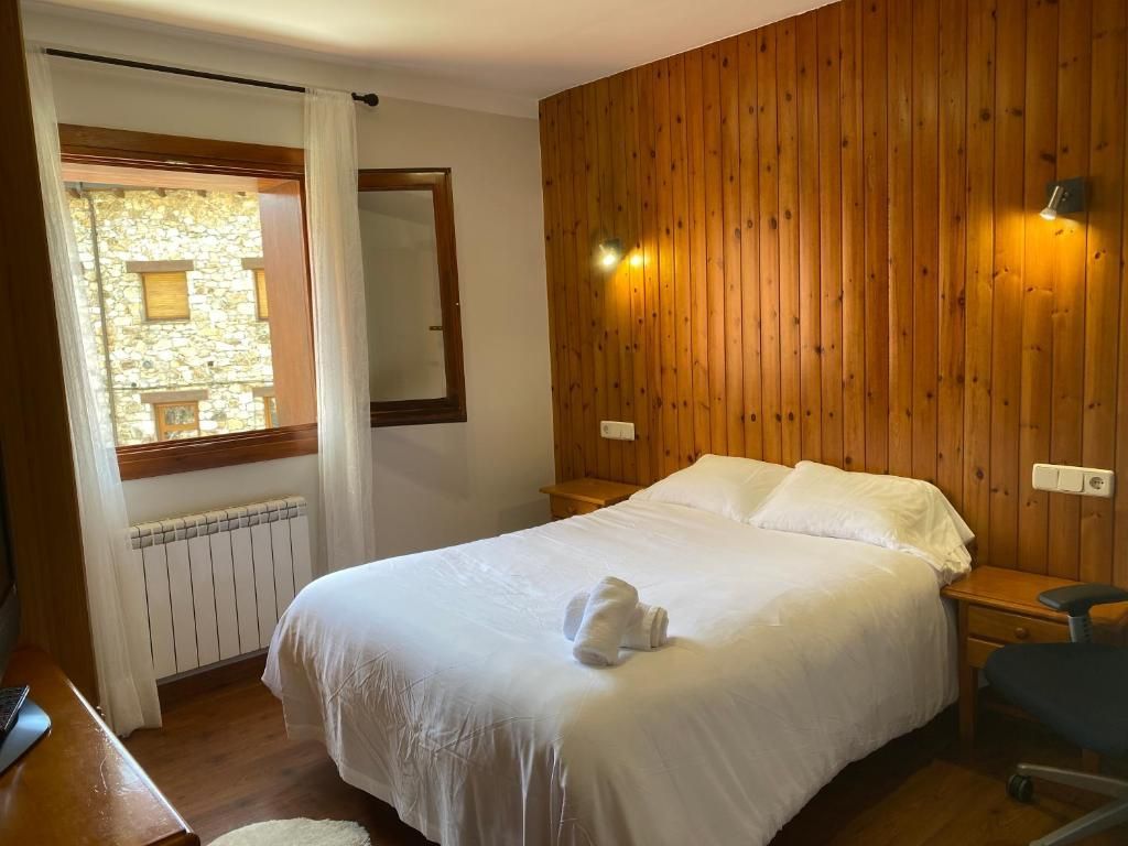 Dormitori amb paret amb panells de fusta, llit doble, finestra amb vistes a la pedra i làmpades de nit.