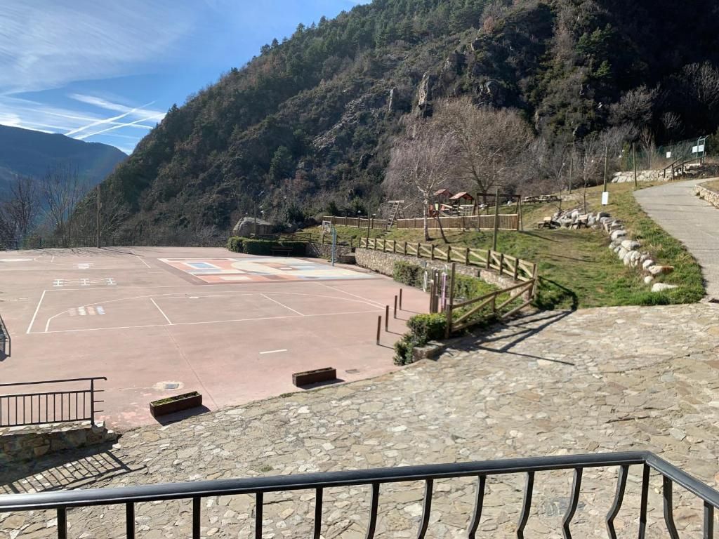 Pista de bàsquet a l'aire lliure amb muntanyes al fons, envoltada per una tanca i un camí.