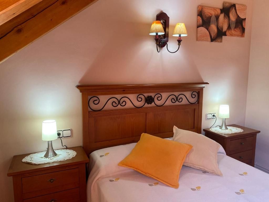 Dormitori amb capçal de fusta, tauletes de nit i làmpades. Aplic de paret i obres d'art sobre el llit.