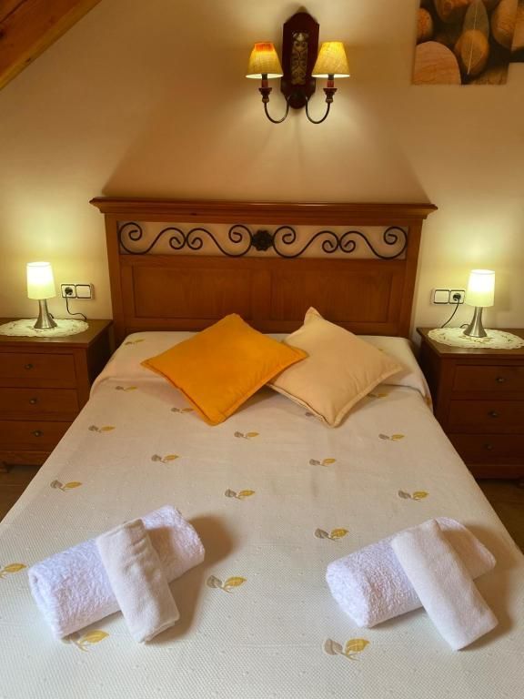 Dormitori amb llit, tauletes de nit, làmpades i capçal decoratiu, dues tovalloles plegades.