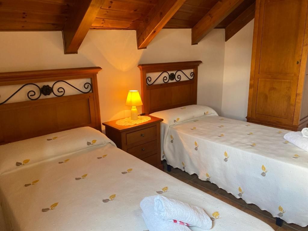 Dos llits individuals en una habitació amb sostre de fusta i una petita tauleta de nit amb un llum.