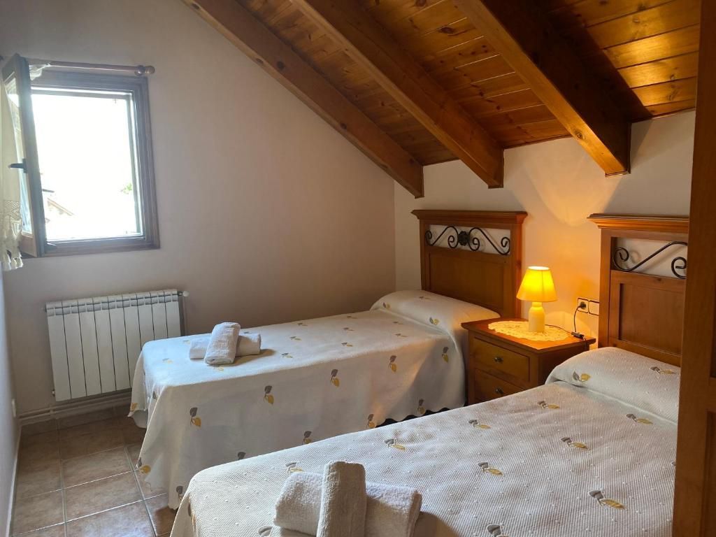 Dormitori amb dos llits individuals, tauleta de nit petita amb làmpada, finestra, radiador. Sostre inclinat de fusta.
