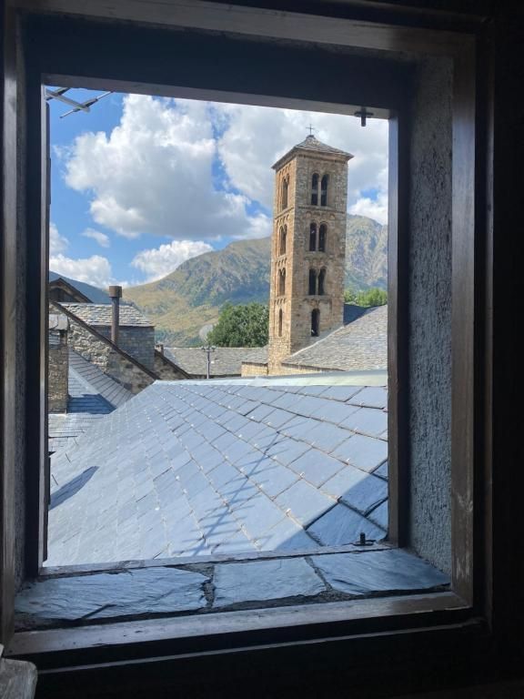 Vista des d'una finestra d'una alta torre de pedra amb muntanyes i cel blau visibles.