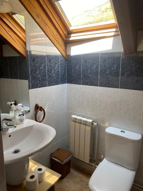 Bany amb lavabo, vàter i radiador blancs. Rajoles blaves i blanques amb claraboia.