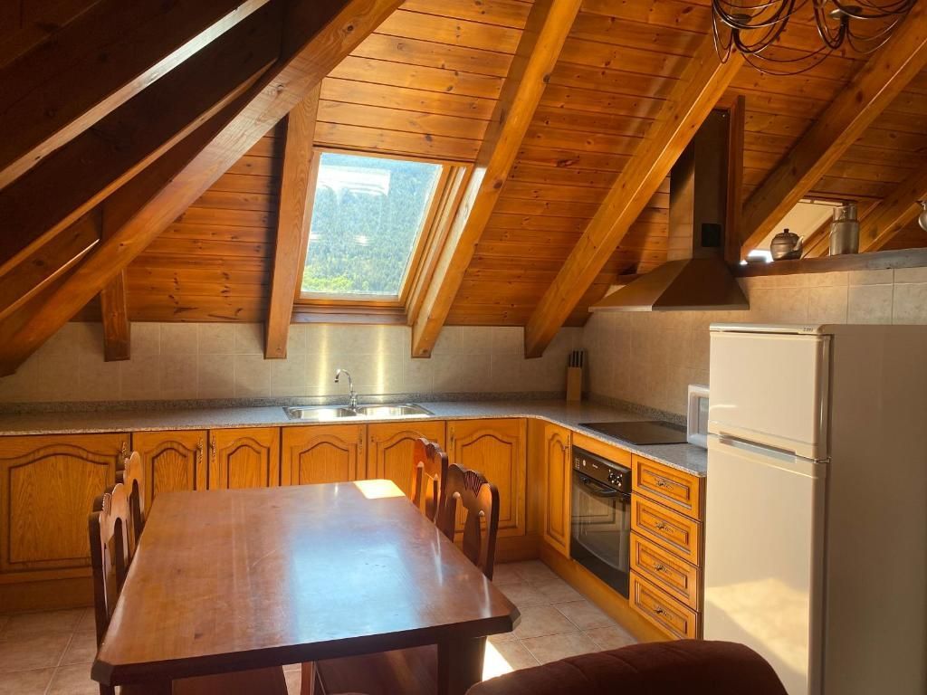 Cuina amb armaris de fusta, sostre inclinat, claraboia, taula de menjador i nevera.