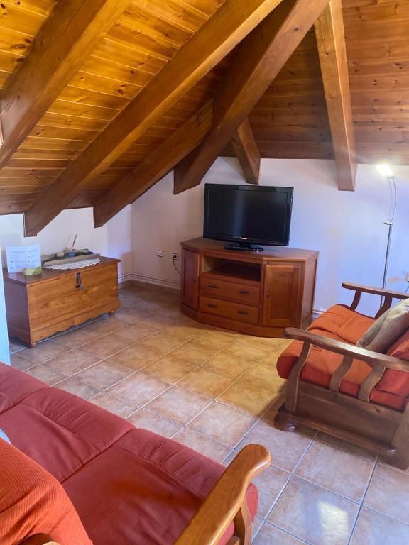 Sala d'estar amb bigues de fusta, televisor sobre un armari de fusta i mobles taronges.