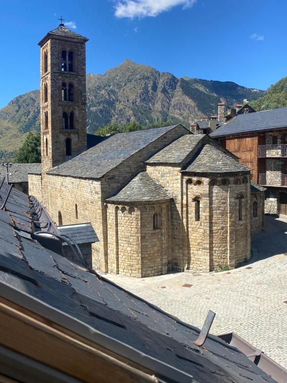 Església de pedra amb un campanar alt, amb una muntanya de fons sota un cel blau.