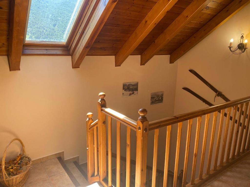 Escala de fusta amb barana i claraboia, que baixa. Esquís i fotos penjats a la paret.