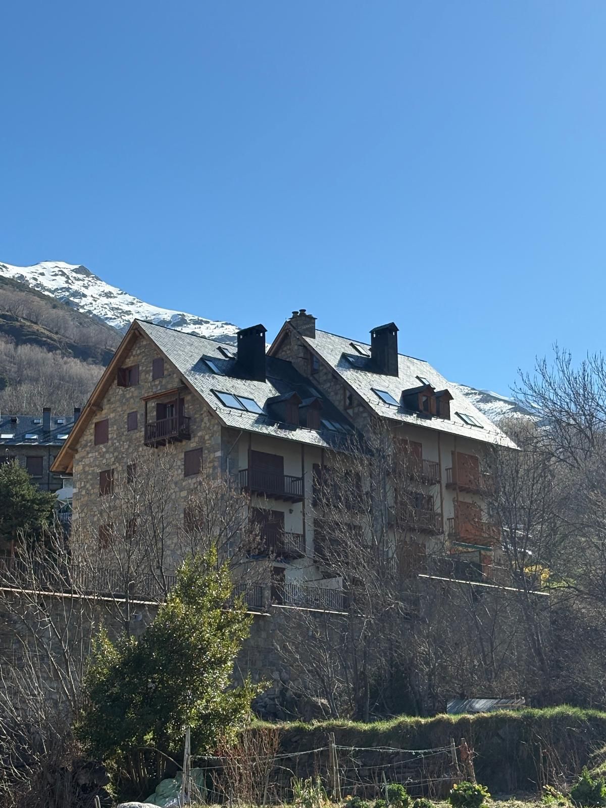 Edifici de pedra amb persianes marrons i un petit balcó contra un cel blau brillant.