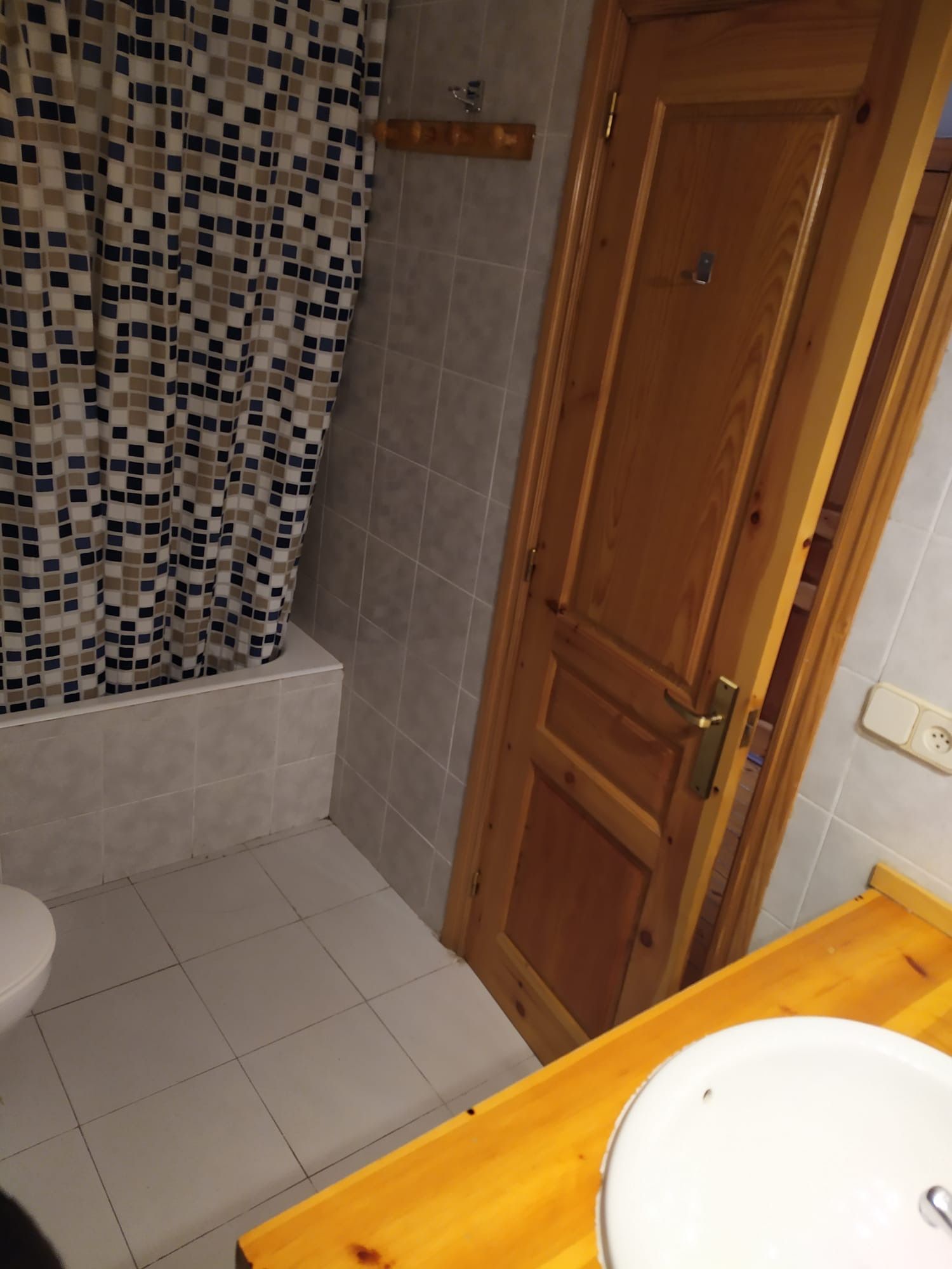 Bany amb cortina de dutxa, porta de fusta i lavabo.