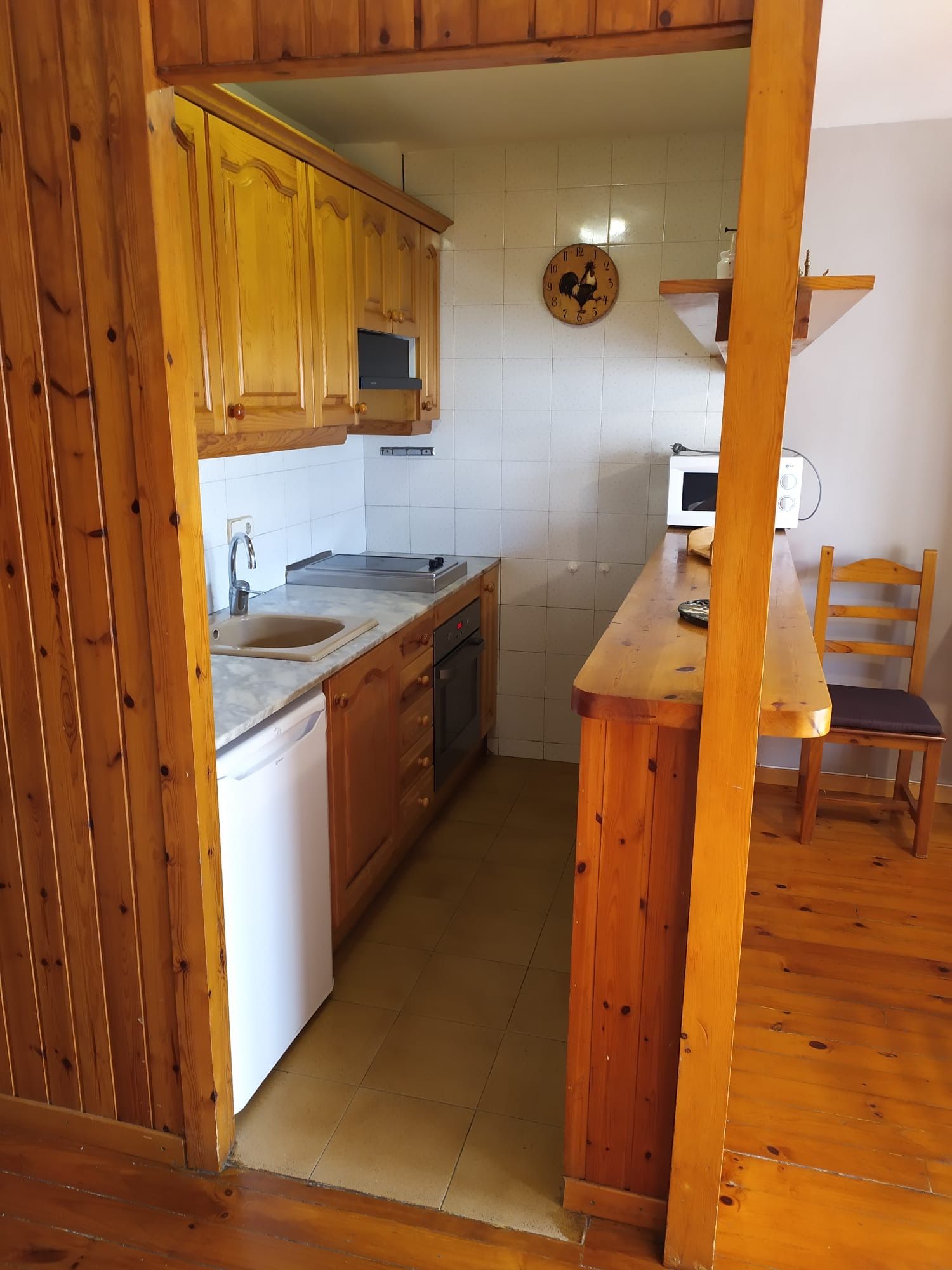 Cuina petita amb armaris de fusta, taulell i electrodomèstics. Vista a través de la porta.