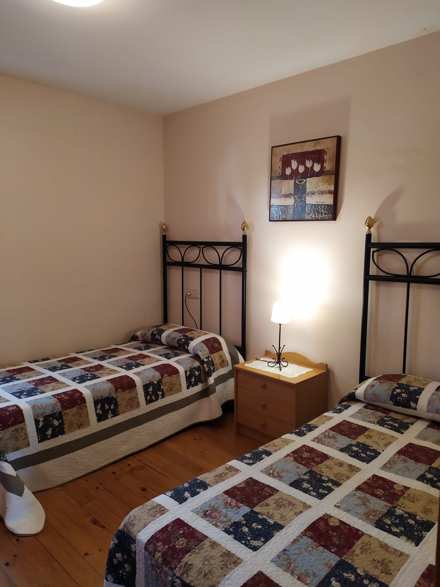 Dos llits individuals amb edredons de patchwork en una habitació amb tauleta de nit i obres d'art.