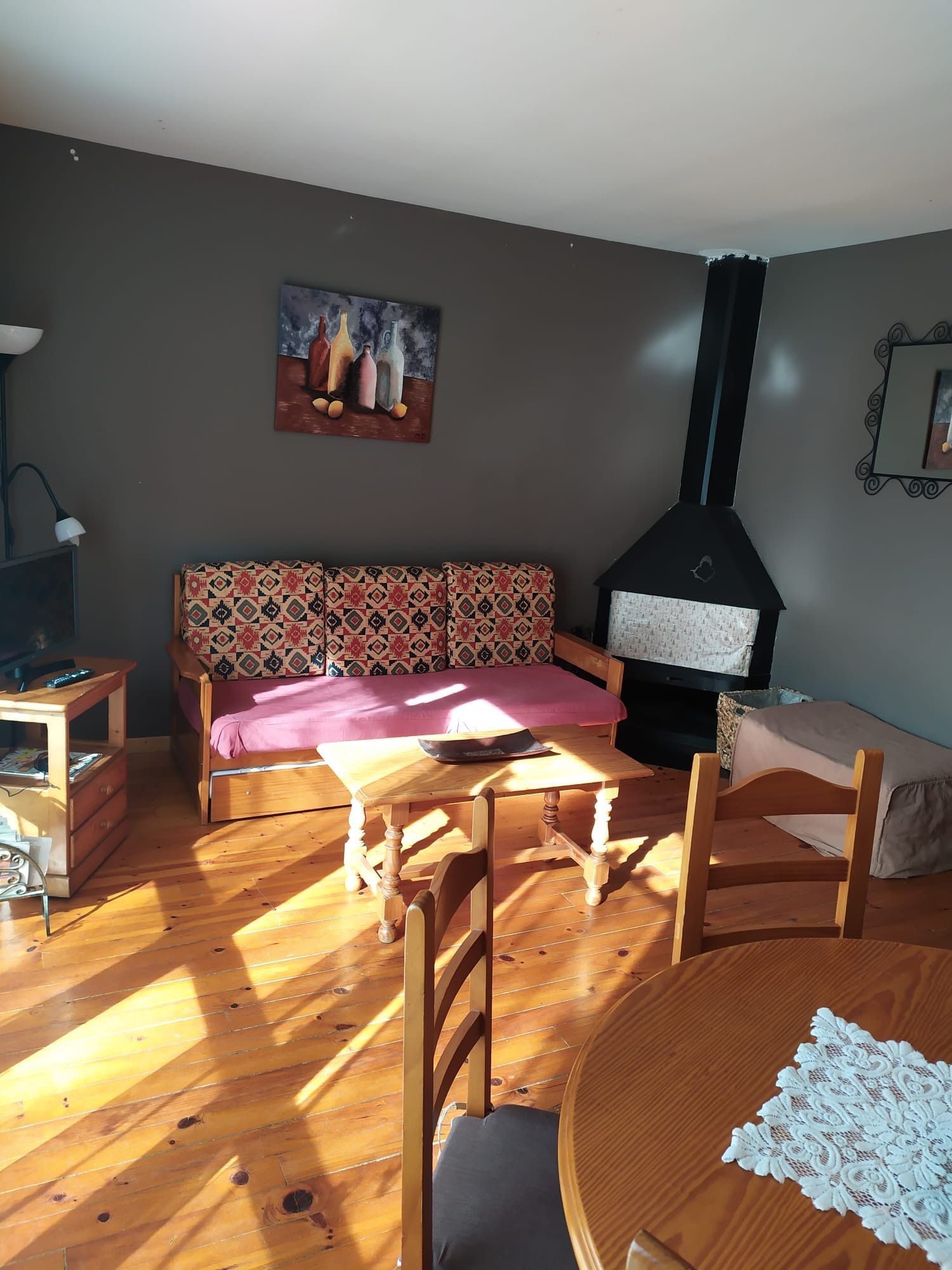 Sala d'estar amb terres de fusta, sofà, llar de foc, taula, cadira, obres d'art i paret grisa.