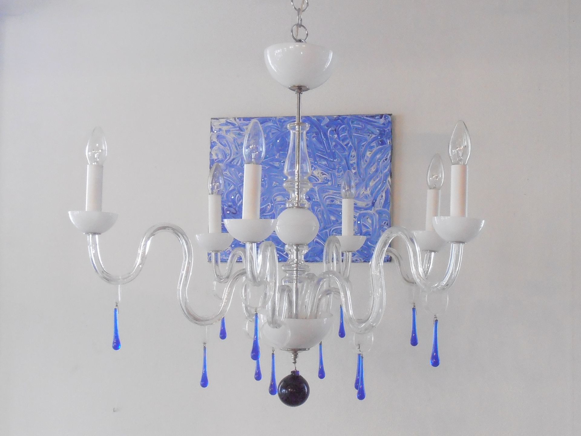 ein weißer Kronleuchter mit blauen Tropfen hängt an einer weißen Wand