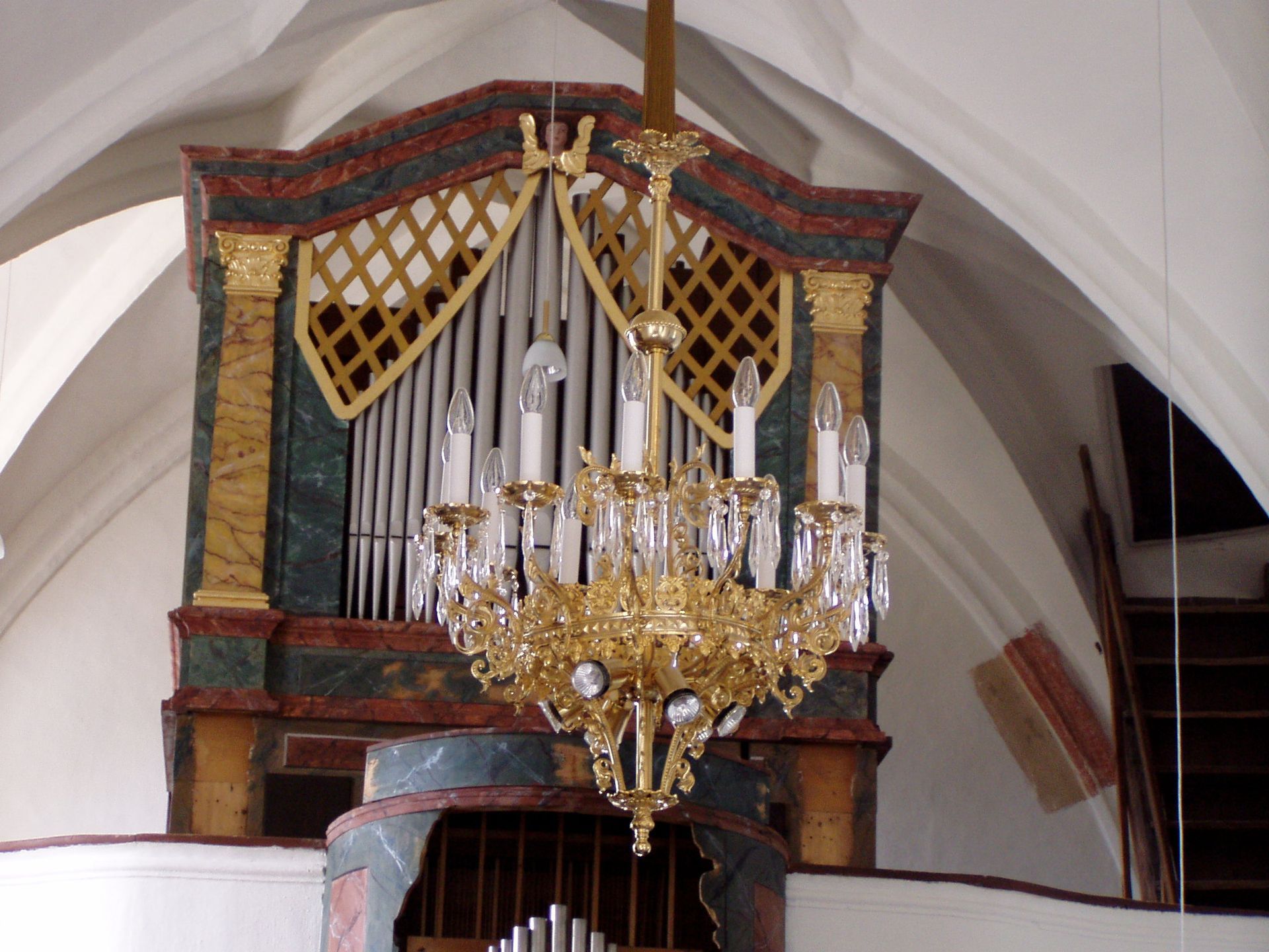 ein goldener Kronleuchter hängt über einer Orgel in einer Kirche