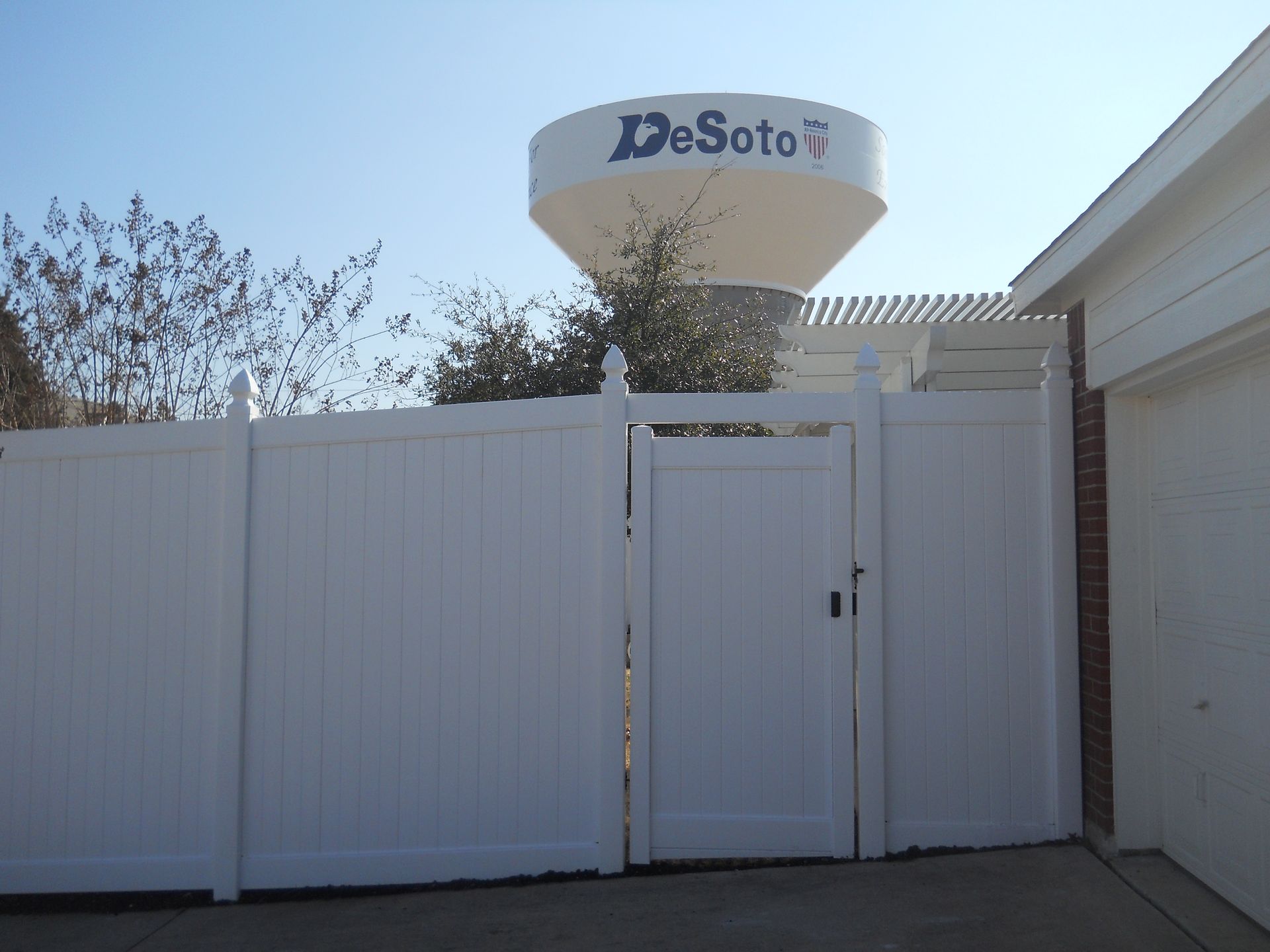 A white fence surrounds a driveway in front of a house