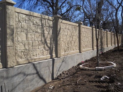 A stone fence is being built in a yard with trees in the background.
