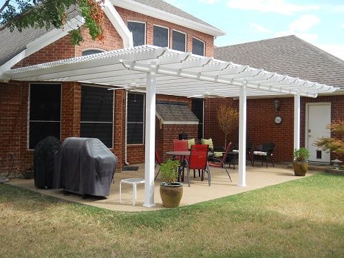 A brick house with a white pergola over a patio with tables and chairs.