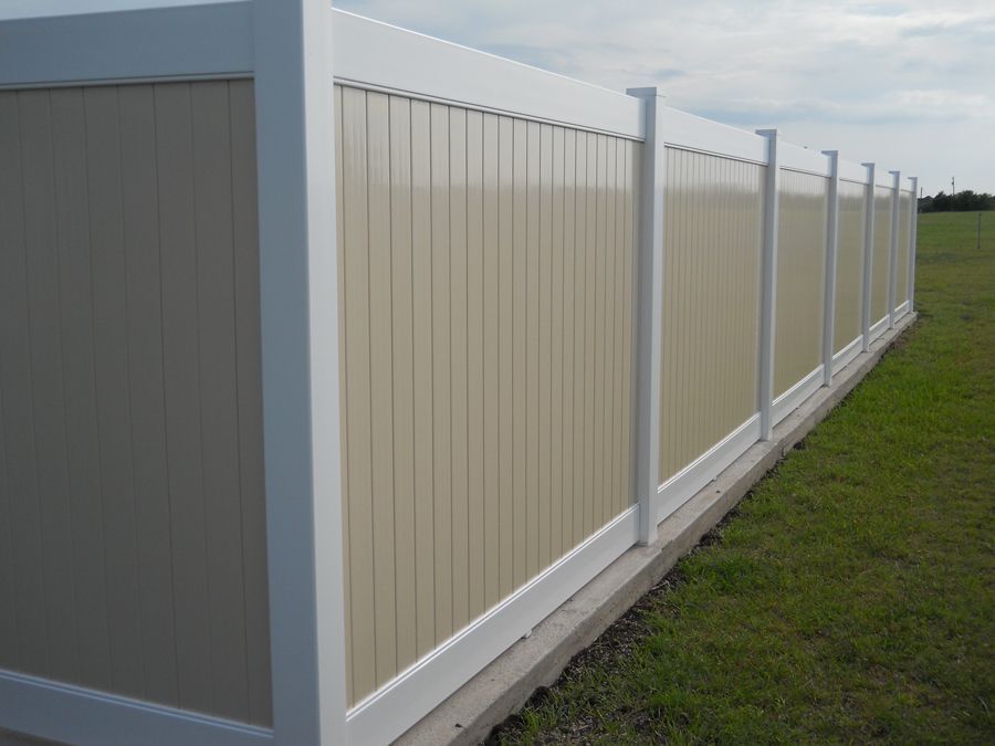 A white and tan fence is sitting in the middle of a grassy field.