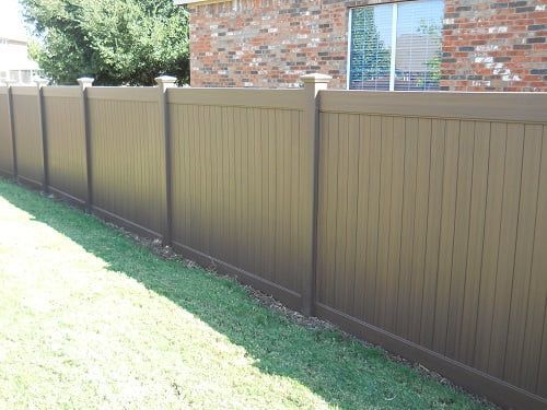 A brown fence surrounds a lush green yard in front of a brick house.