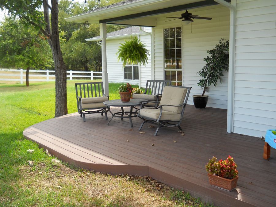 A deck with chairs and a table in front of a white house