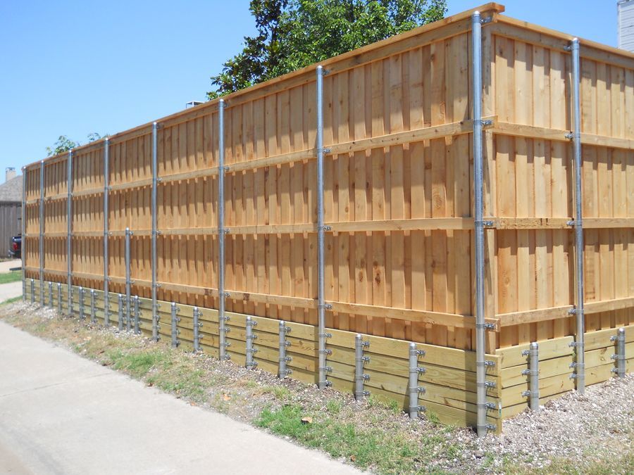 A wooden fence with metal posts is sitting next to a sidewalk.