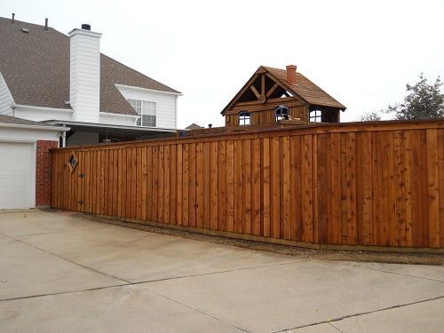 A wooden fence surrounds a driveway in front of a house.