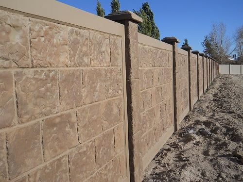 A brick fence is surrounded by dirt and trees