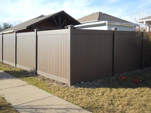 A brown fence is sitting next to a sidewalk in front of a house.