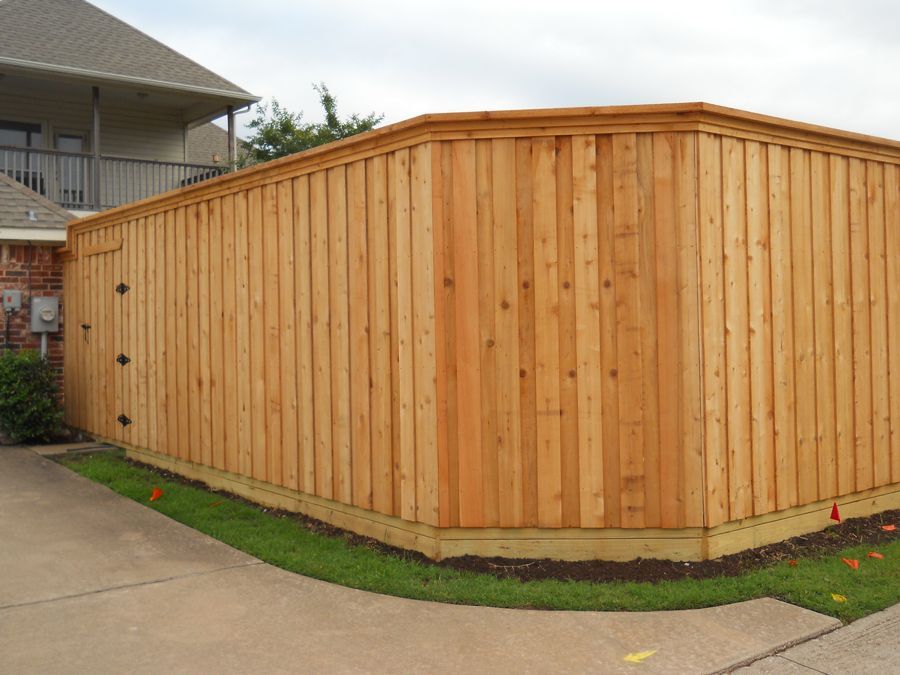 A wooden fence is sitting on the side of a driveway next to a house.
