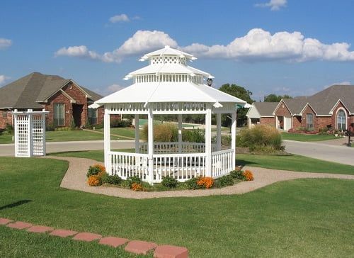 A white gazebo sits in the middle of a lush green yard