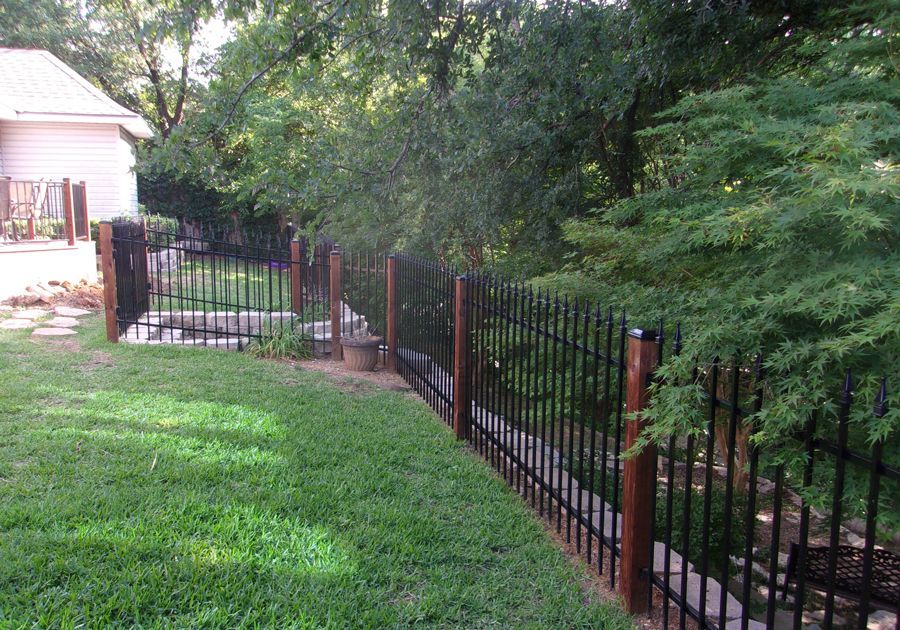 A wrought iron fence surrounds a lush green yard.