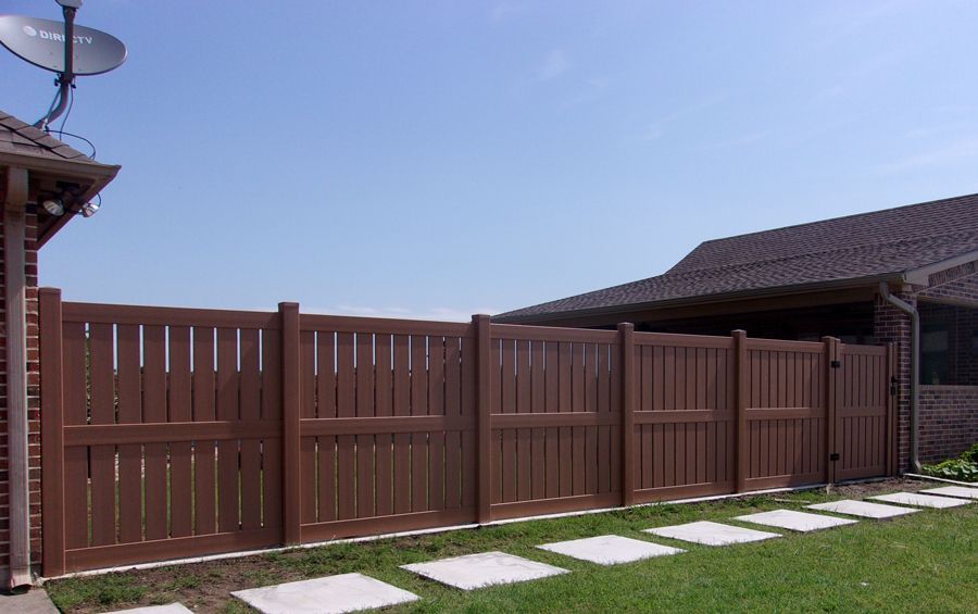 A wooden fence surrounds a lush green yard in front of a house.
