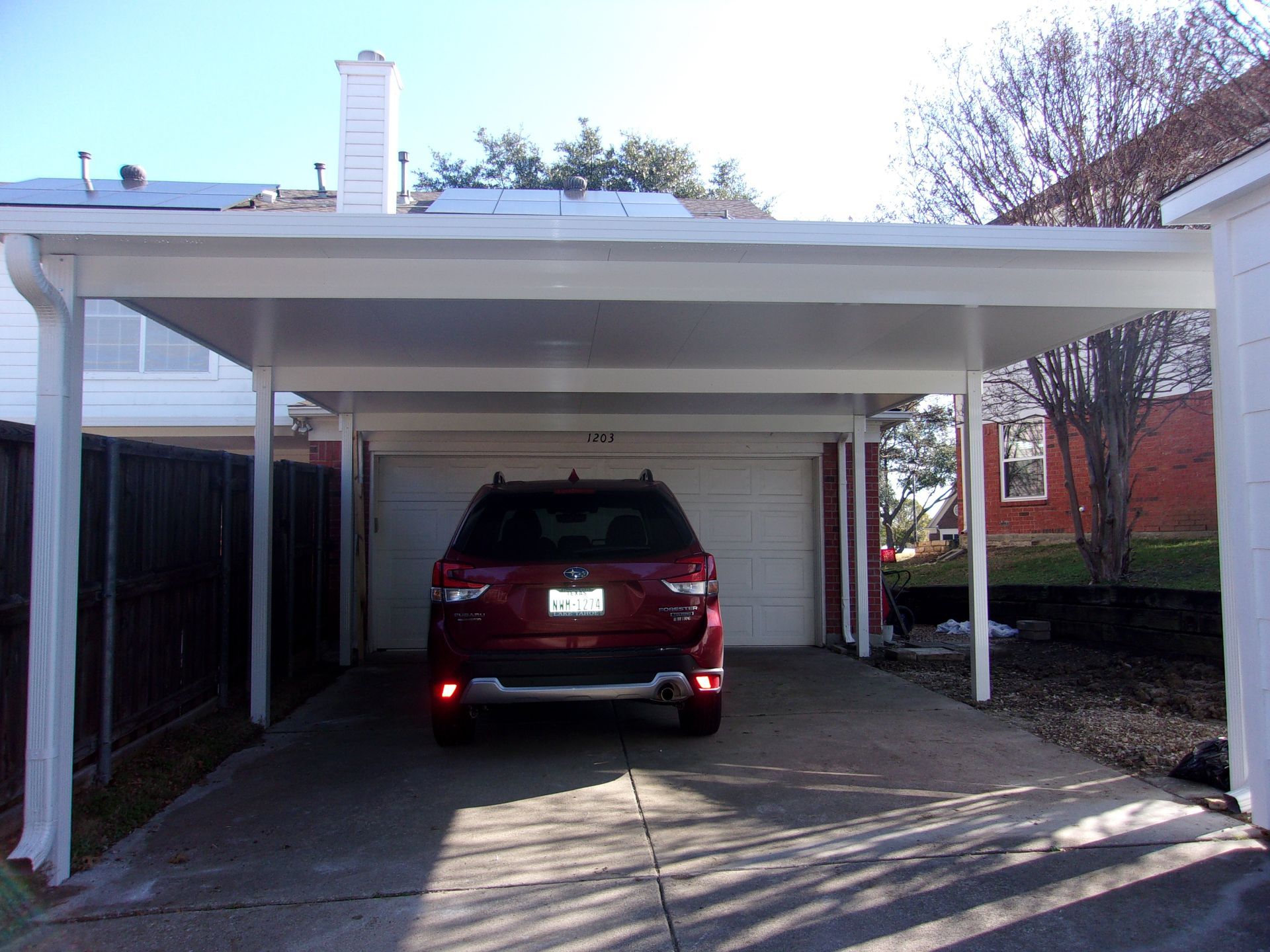 A white pergola is sitting on top of a brick patio next to a house.