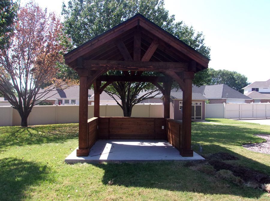 A wooden gazebo sits in the middle of a lush green yard