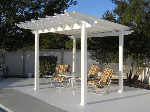 A white pergola with a table and chairs underneath it