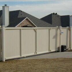 A white fence is surrounding a driveway in front of a house.