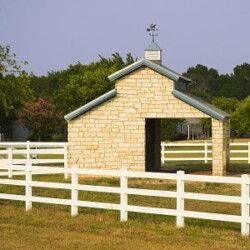 A white fence surrounds a stone building in a field.