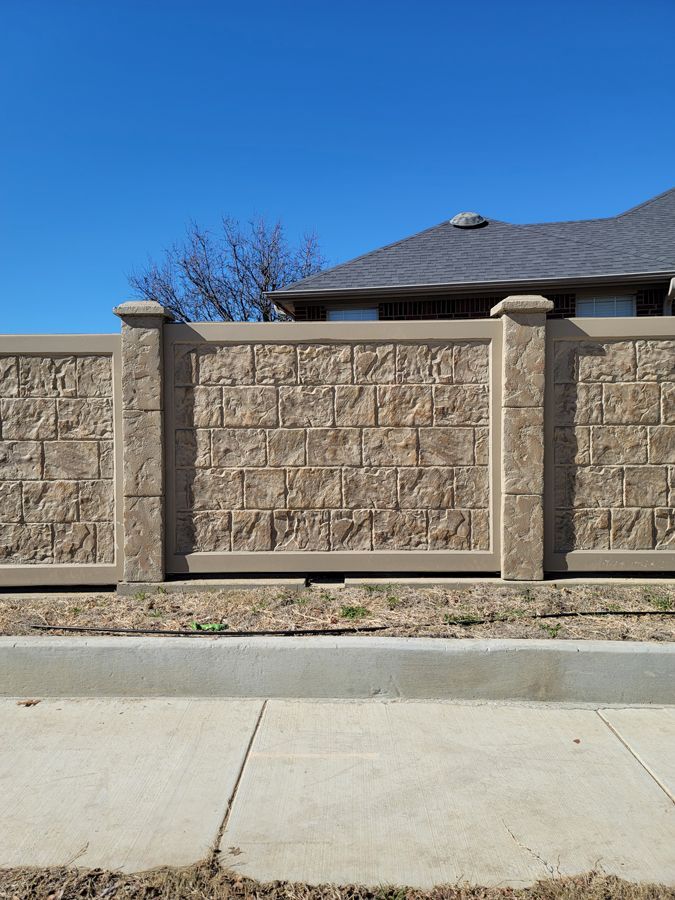 A brick fence surrounds a house on a sunny day.