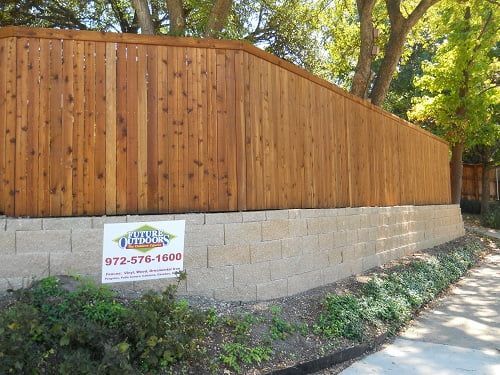A wooden fence is surrounded by trees and a brick wall.