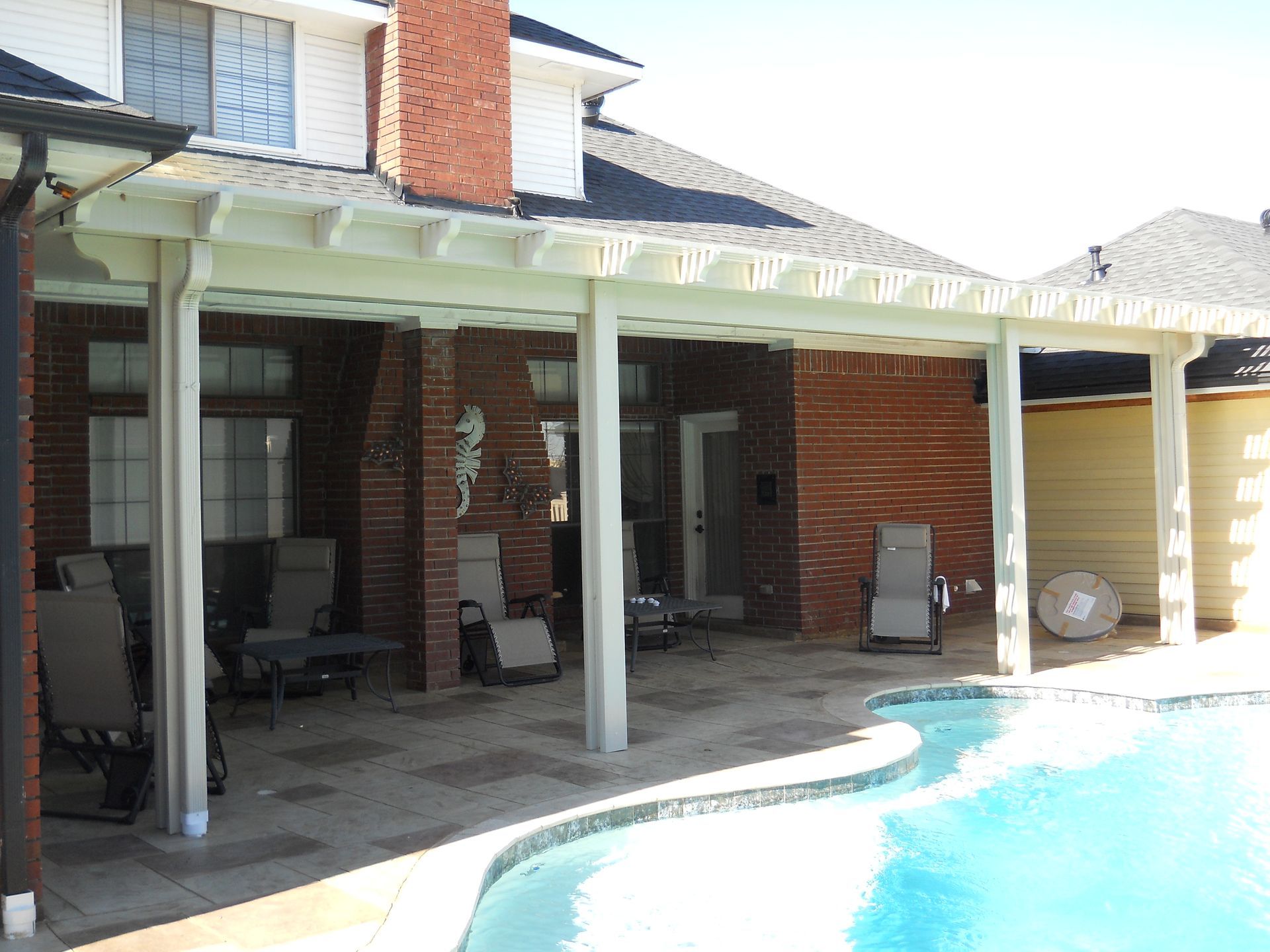 A white pergola over a swimming pool with a table and chairs underneath it