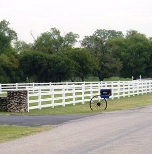 A horse drawn carriage is parked in front of a white fence.