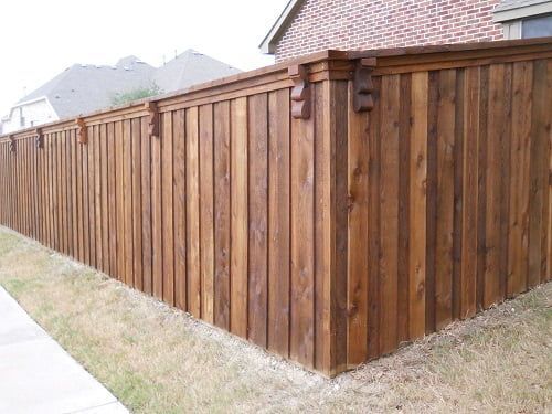 A wooden fence is sitting next to a sidewalk in front of a brick house.