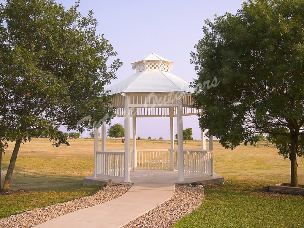A white gazebo sits in the middle of a grassy field