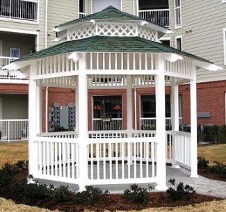 A white gazebo with a green roof in front of a building