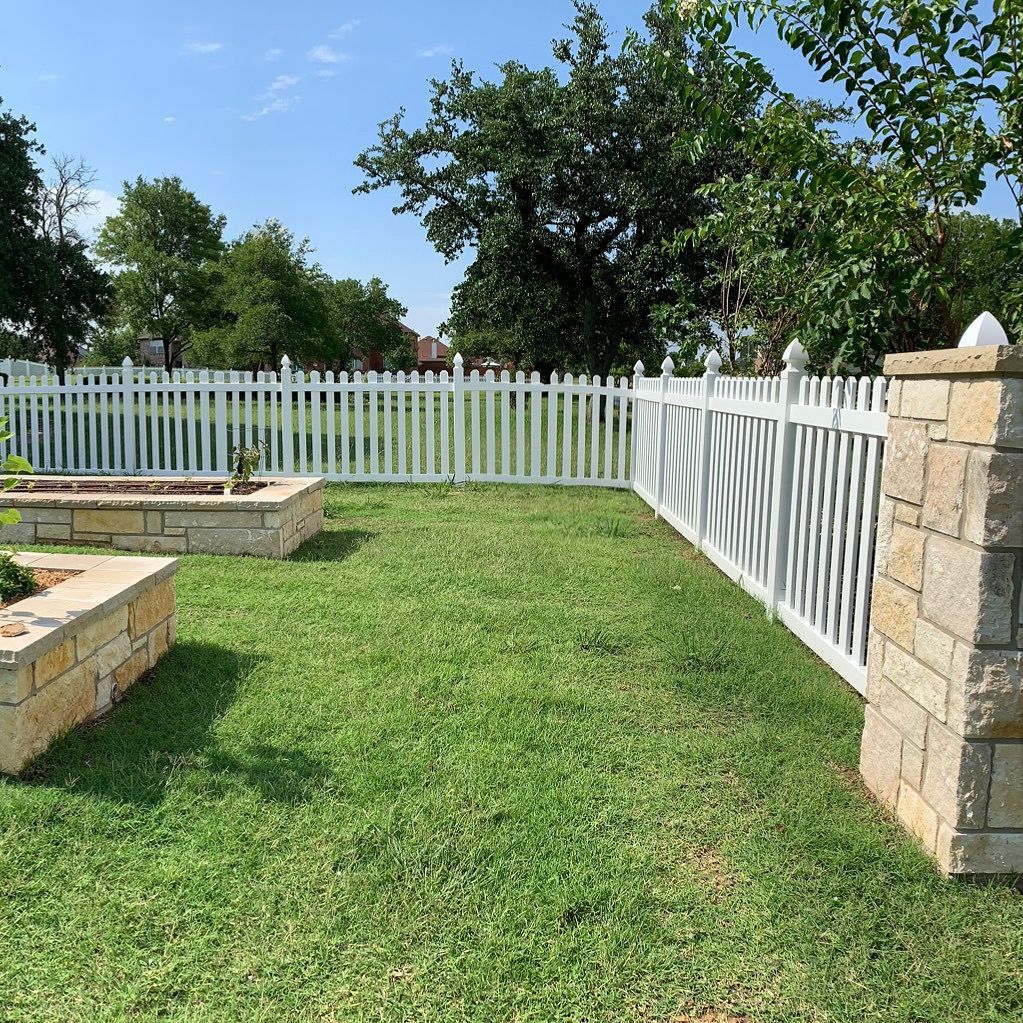 A backyard with a white picket fence and a fire pit.