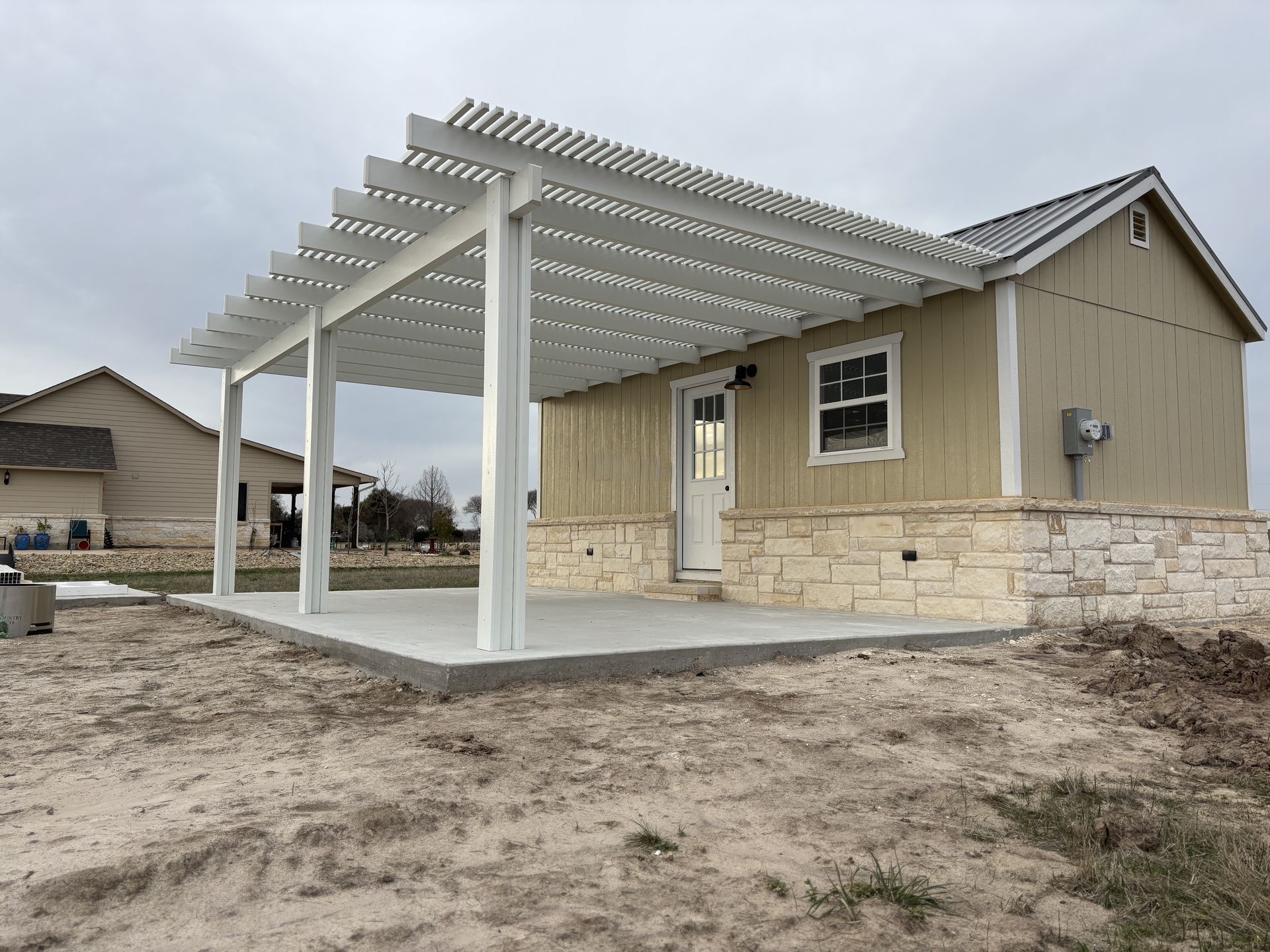 A white pergola is sitting on top of a patio next to a house.